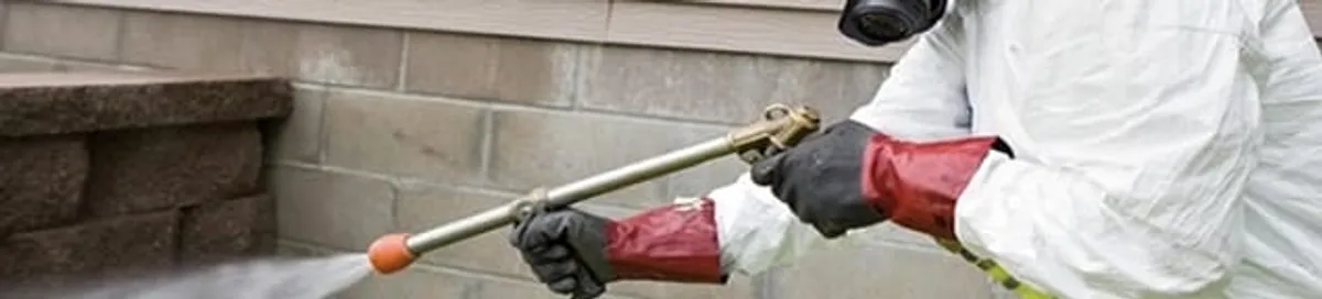 Pest control technician applying exterior insect treatment along a home foundation in Chattanooga, TN