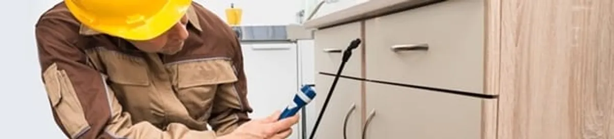 Roach exterminator applying treatment under kitchen cabinets in Chattanooga, TN