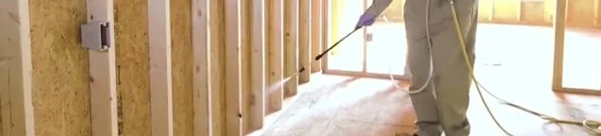 Termite treatment technician applying spray along framing and unfinished walls in Chattanooga, TN